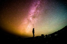 Un homme de profil, debout, regarde au-dessus de lui un ciel étoilé et coloré